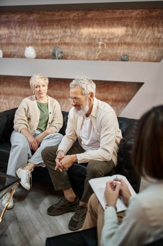 middle aged married couple sitting on couch and discussing problem near psychologist during session middle aged married couple sitting on couch and discussing problem near psychologist during session